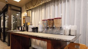 A breakfast bar with cereal dispensers, a coffee machine, and a stack of white plates.