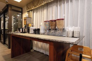 A breakfast bar with cereal dispensers, a coffee machine, and a stack of white plates.