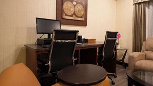 A hotel room with two desks, two chairs, a round table, a sofa, and a wall-mounted globe artwork.
