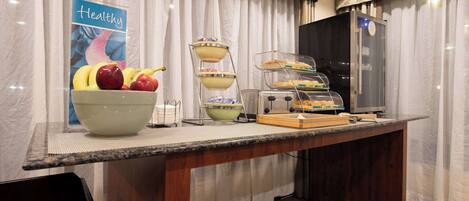 A breakfast bar with a fruit bowl, a tiered serving station, and a refrigerator.
