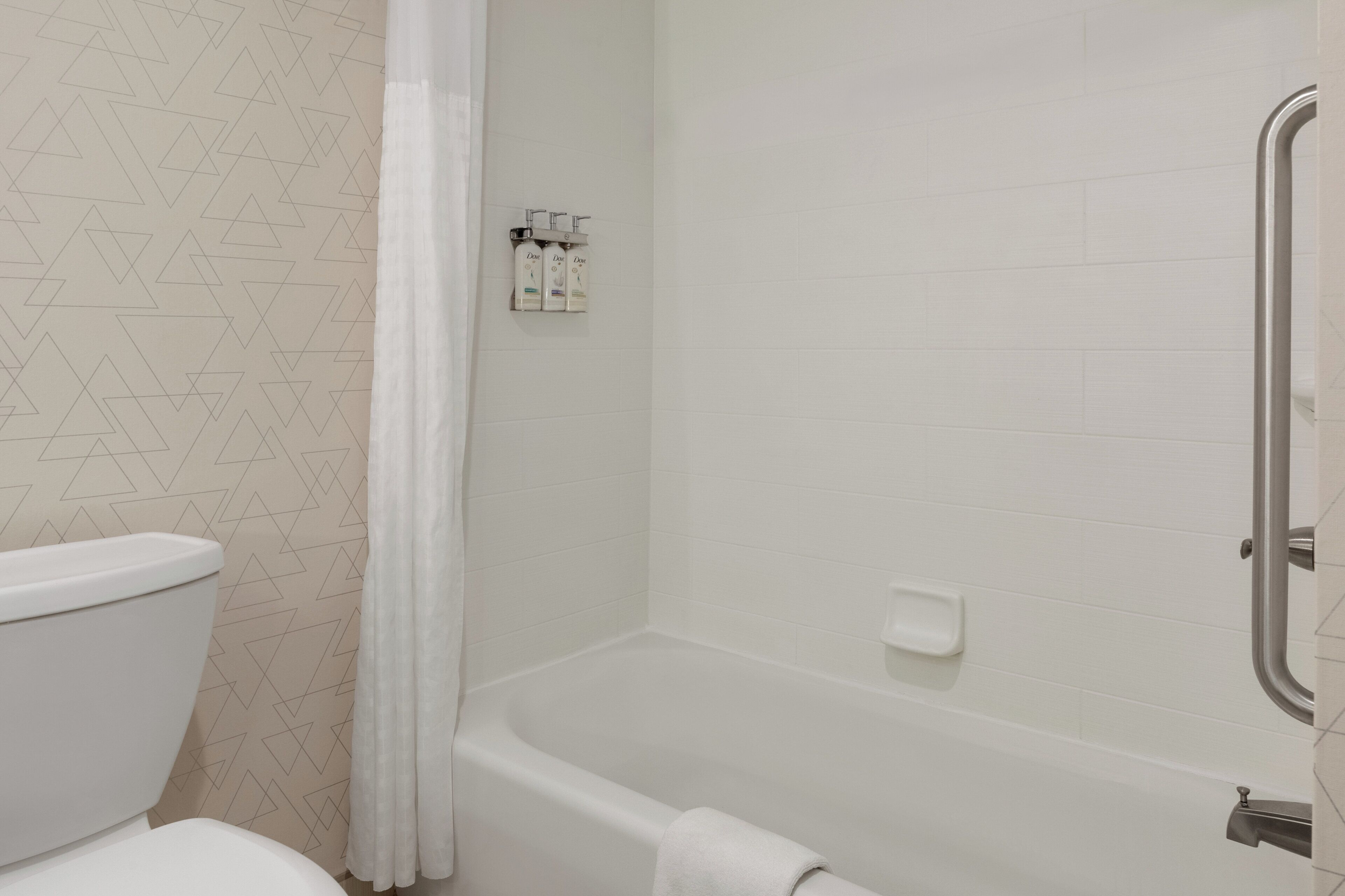 Une salle de bain comprenant des toilettes, une douche équipée d’une barre d’appui et un porte-serviettes.