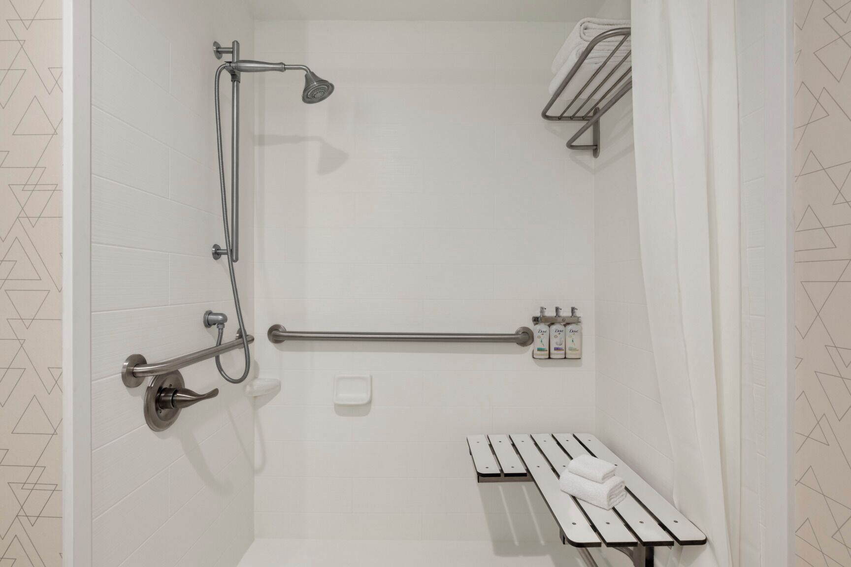 A shower with a handheld showerhead, grab bars, a bench, and a towel rack.