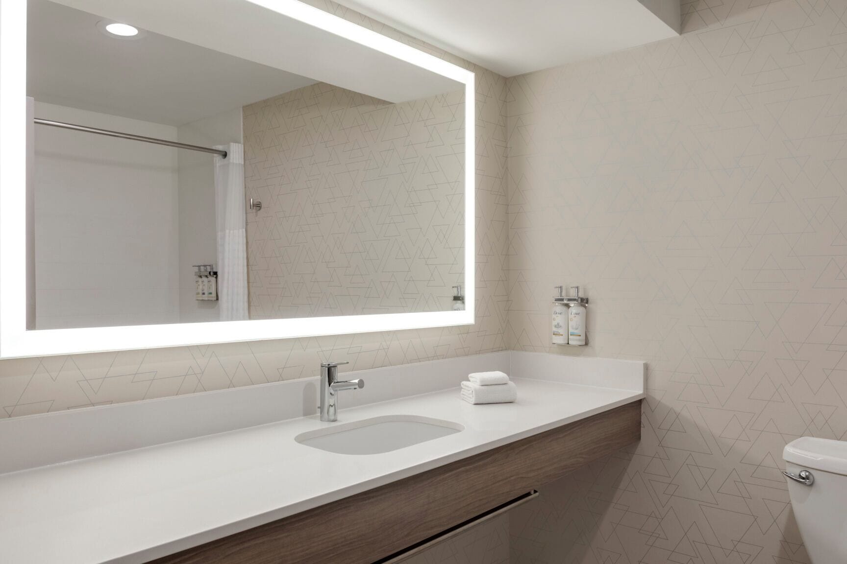 A modern bathroom with a large mirror, a sink, and a toilet.