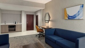Een moderne hotelkamer met een kitchenette, een bank, een bureau en een groot abstract schilderij aan de muur.