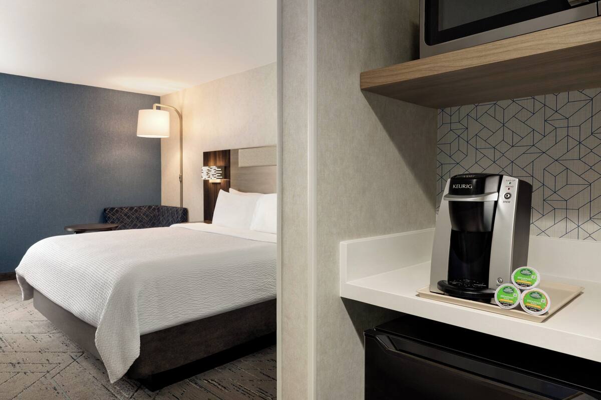 A hotel room with a bed, a coffee maker, and a microwave on the counter.