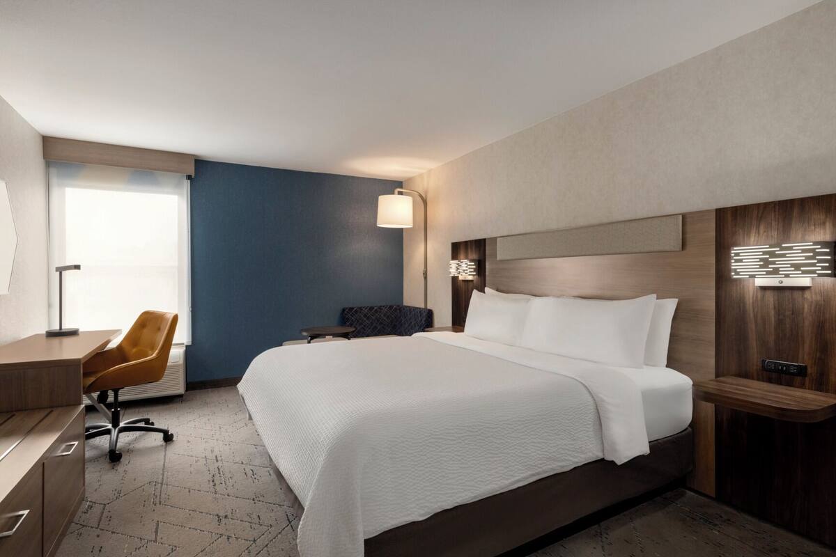 A hotel room with a large bed, a desk, a chair, and a nightstand.