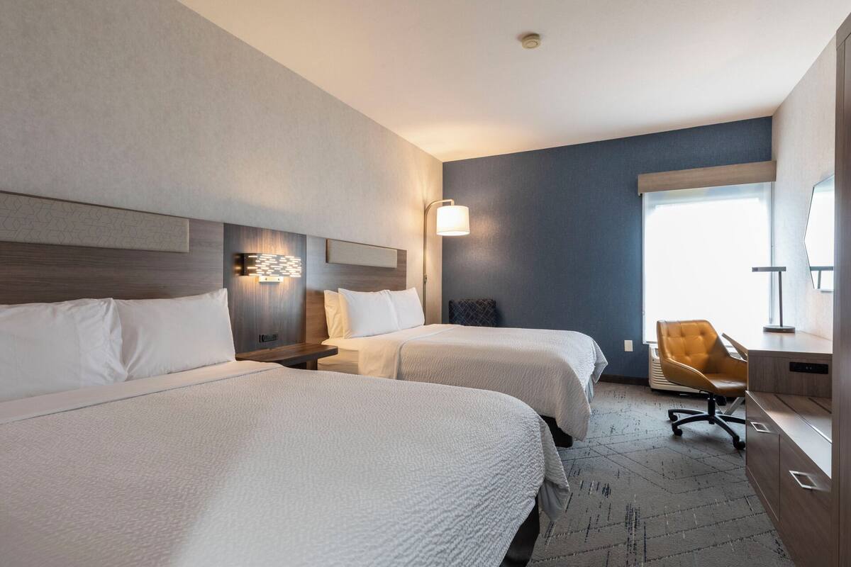 A hotel room with two beds, a desk, a chair, and a large window.