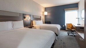 A hotel room with two beds, a desk, a chair, and a large window.