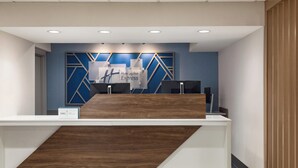 Een receptiebalie met een blauw-wit geometrisch wandontwerp, een houten accent en een bord met 'Holly Inn Express'.