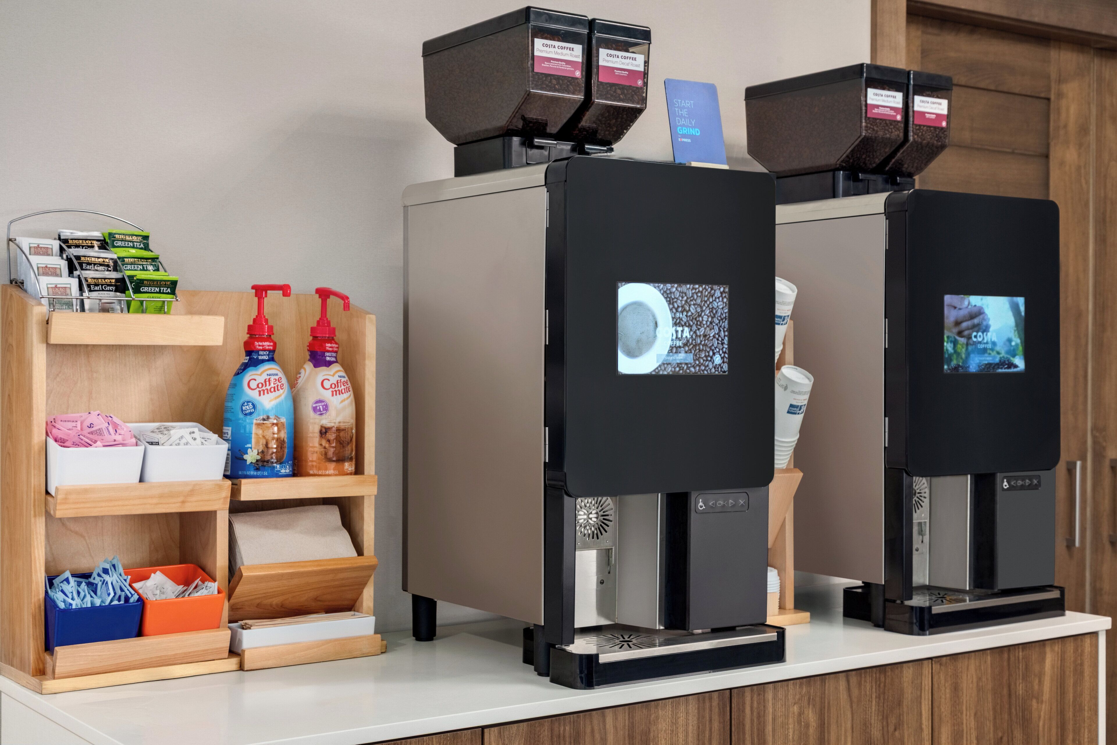 Two coffee machines with digital displays, a shelf with coffee pods, and a counter with a coffee cup.