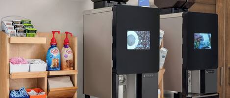 Two coffee machines with digital displays, a shelf with coffee pods, and a counter with a coffee cup.