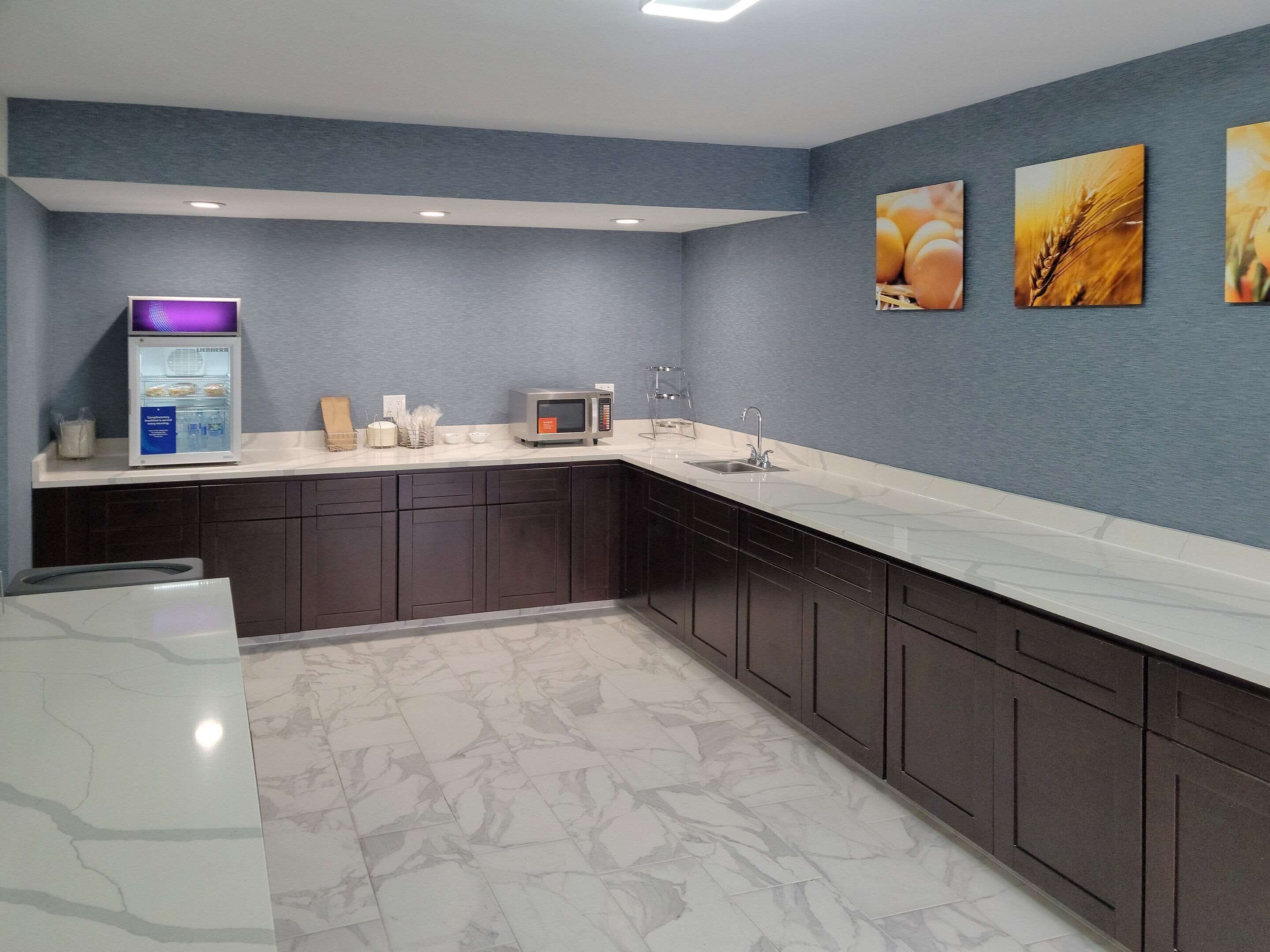 A modern kitchen with dark cabinets, a marble countertop, a microwave, a refrigerator, and three wall-mounted pictures.