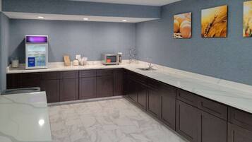 A modern kitchen with dark cabinets, a marble countertop, a microwave, a refrigerator, and three wall-mounted pictures.