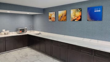 Una cocina moderna con armarios oscuros, una encimera blanca, un microondas y un lavabo. Hay cuatro cuadros en la pared.
