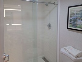 Una ducha con cerramiento de vidrio de diseño moderno, un perchero con una toalla doblada y un cuadro en la pared.