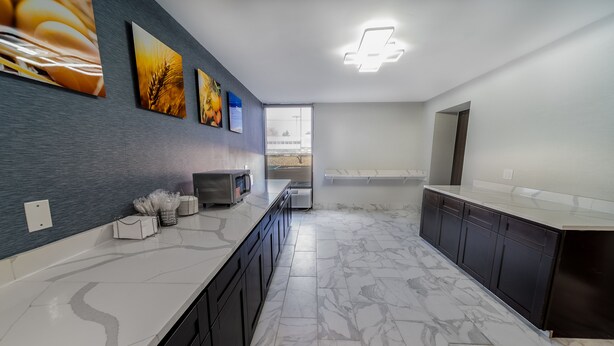 A modern kitchen with marble flooring, dark cabinetry, and a large window providing a view of the outdoors.