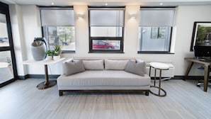 A modern living room with a sofa, a small table, and a large window with a view of a red car outside.