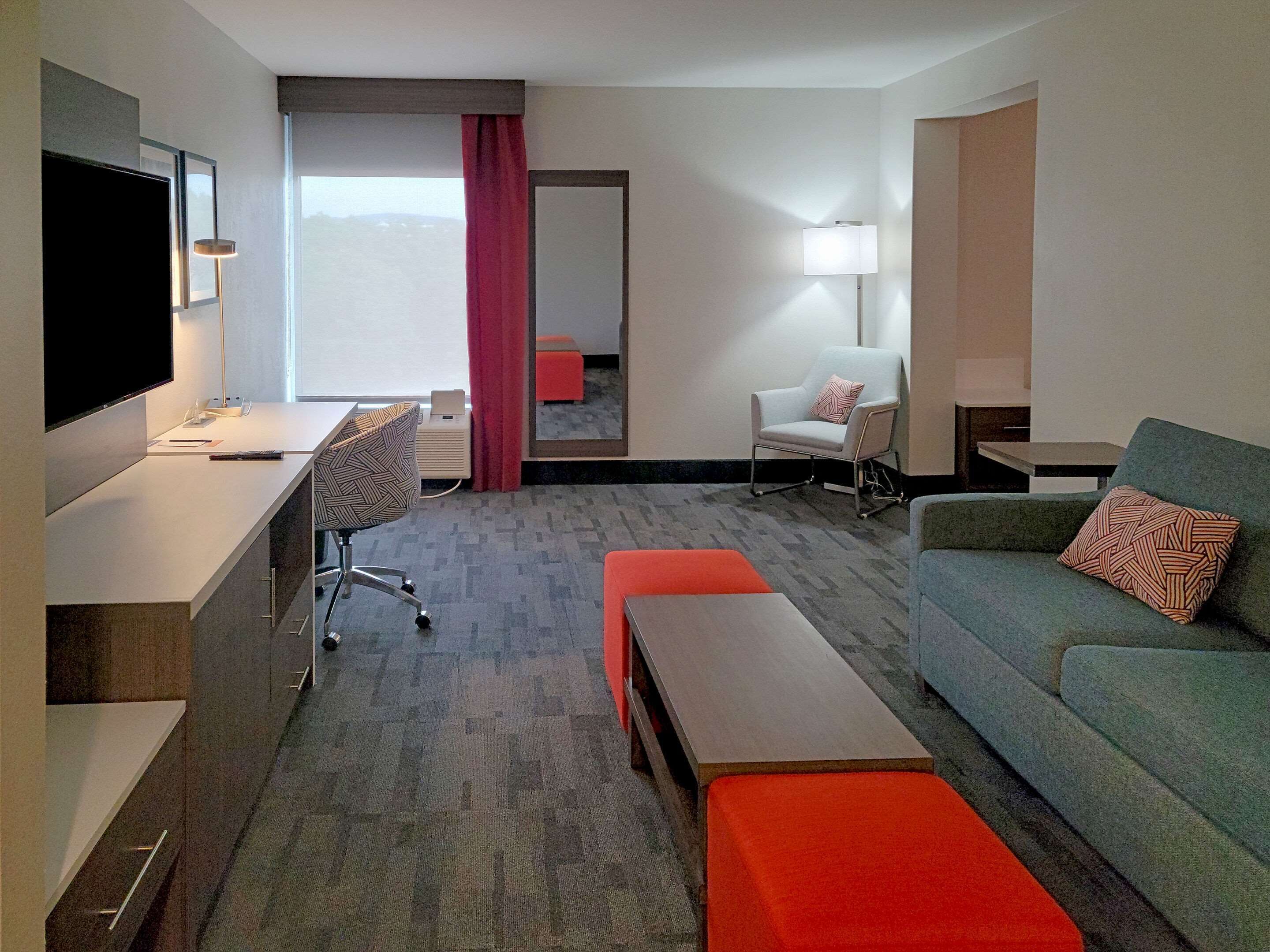 Una habitación de hotel con escritorio, una silla, un sofá y un televisor.