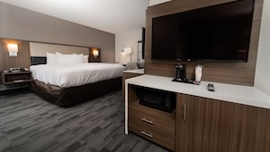 A hotel room with two beds, a flat-screen TV, a microwave, and a bedside table with a lamp.