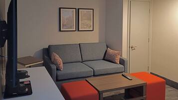 A modern living room with a grey sofa, two framed pictures on the wall, a TV, and a small table with a remote control.