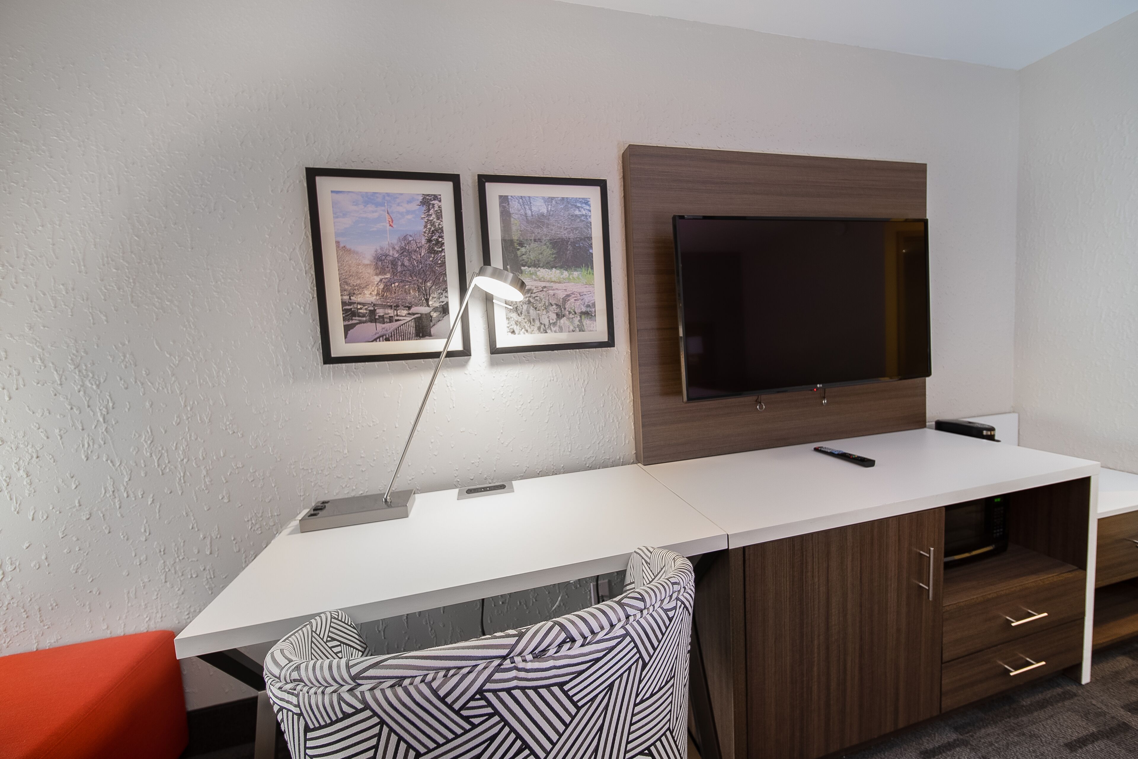 A modern room with a white desk, a mounted TV, and framed pictures on the wall.
