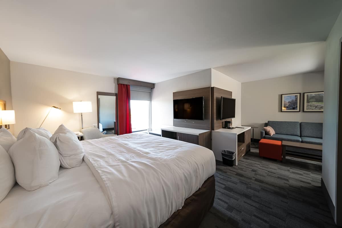 A modern hotel room with a large bed, a desk, a TV, a sofa, and a red curtain.