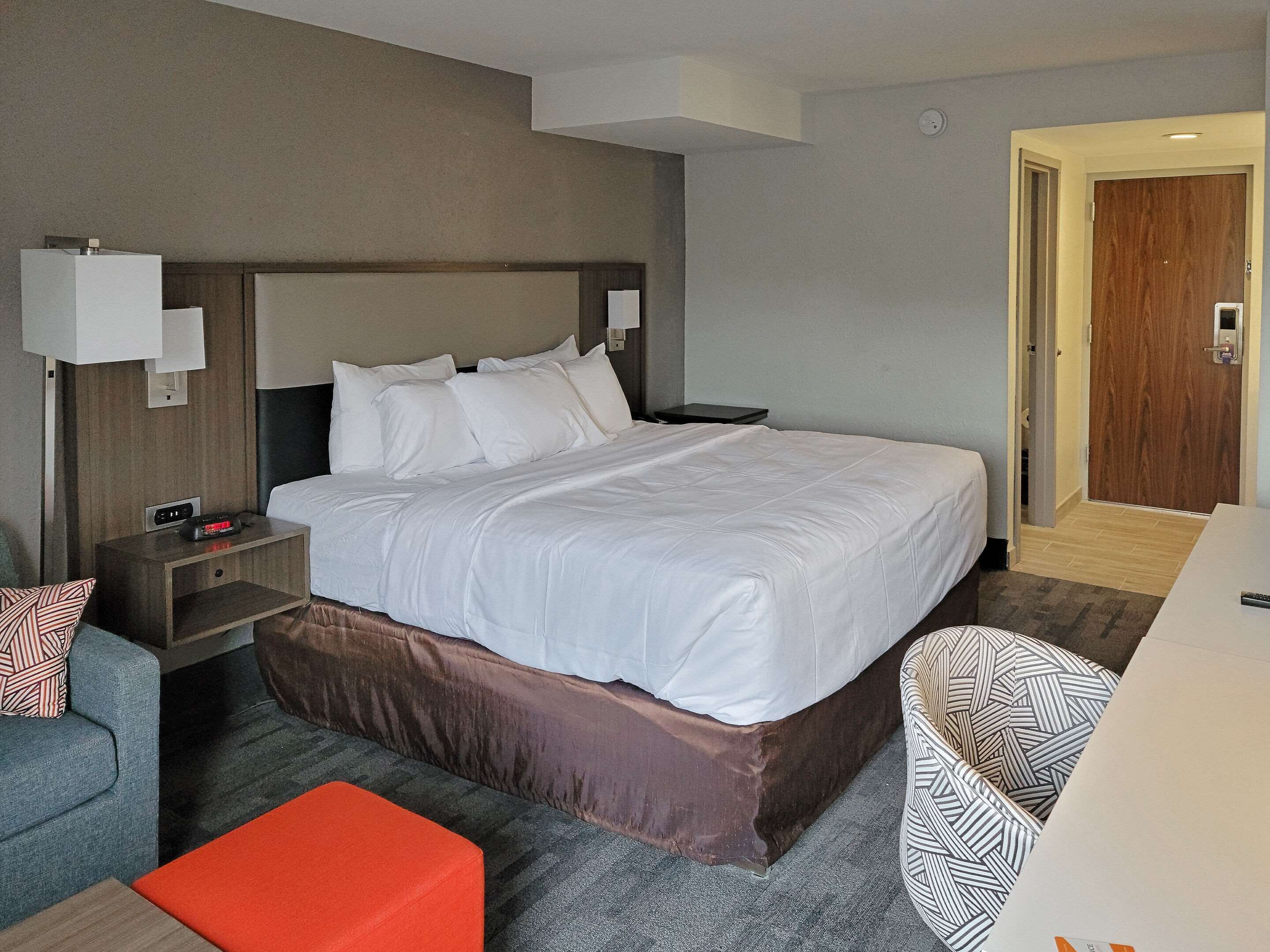 A hotel room with a large bed, a nightstand, a desk, a chair, and a small table.