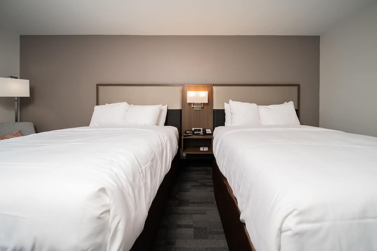 A hotel room with two single beds, a nightstand with a lamp, and a wall-mounted light fixture.
