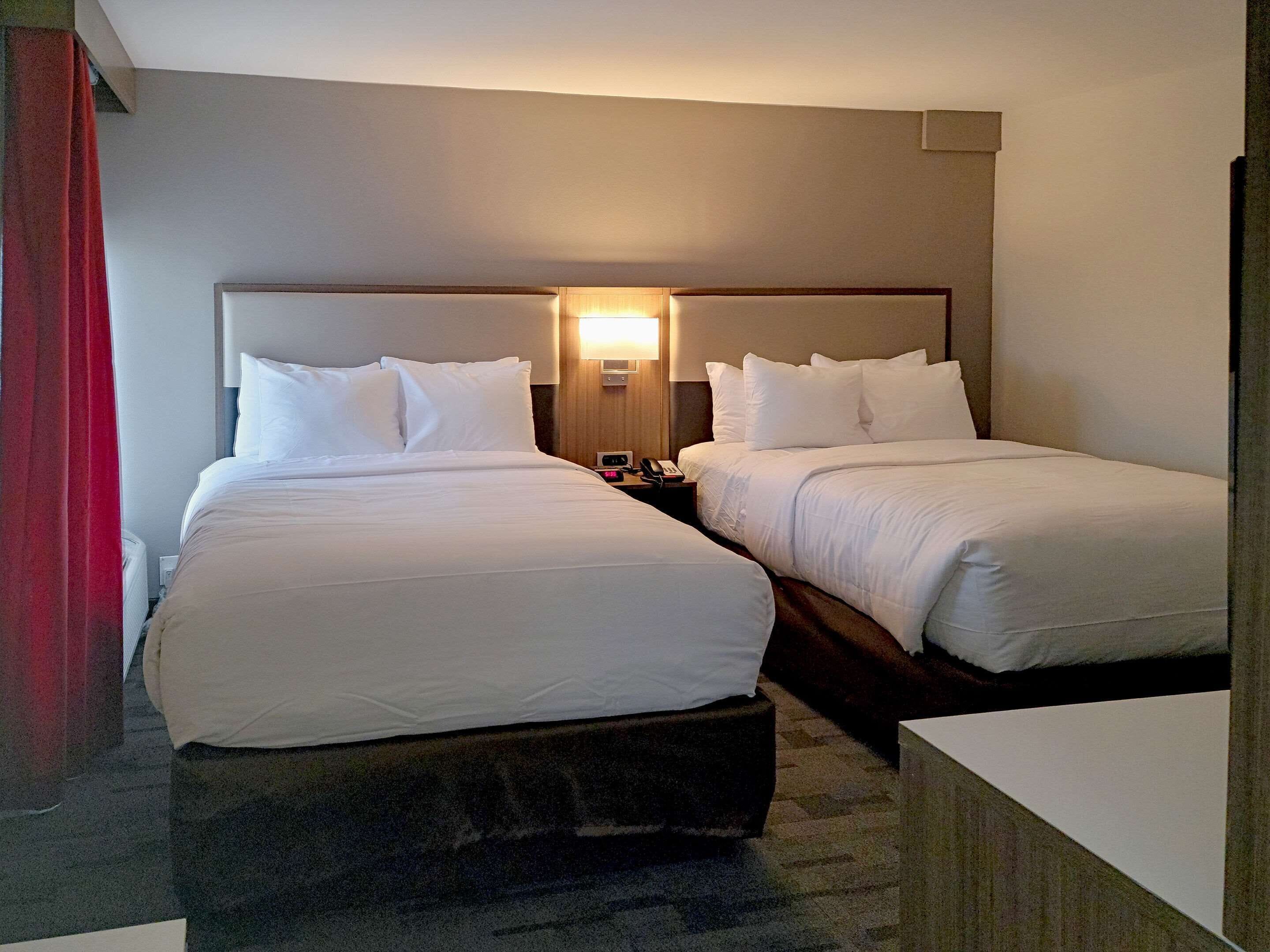Habitación de hotel con dos camas, una mesita de noche con lámpara y una cortina roja.
