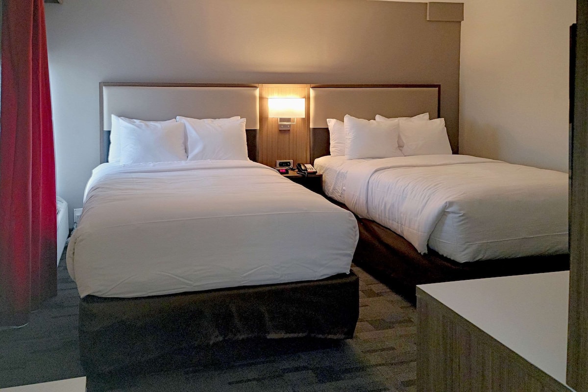 A hotel room with two beds, a bedside table with a lamp, and a red curtain.
