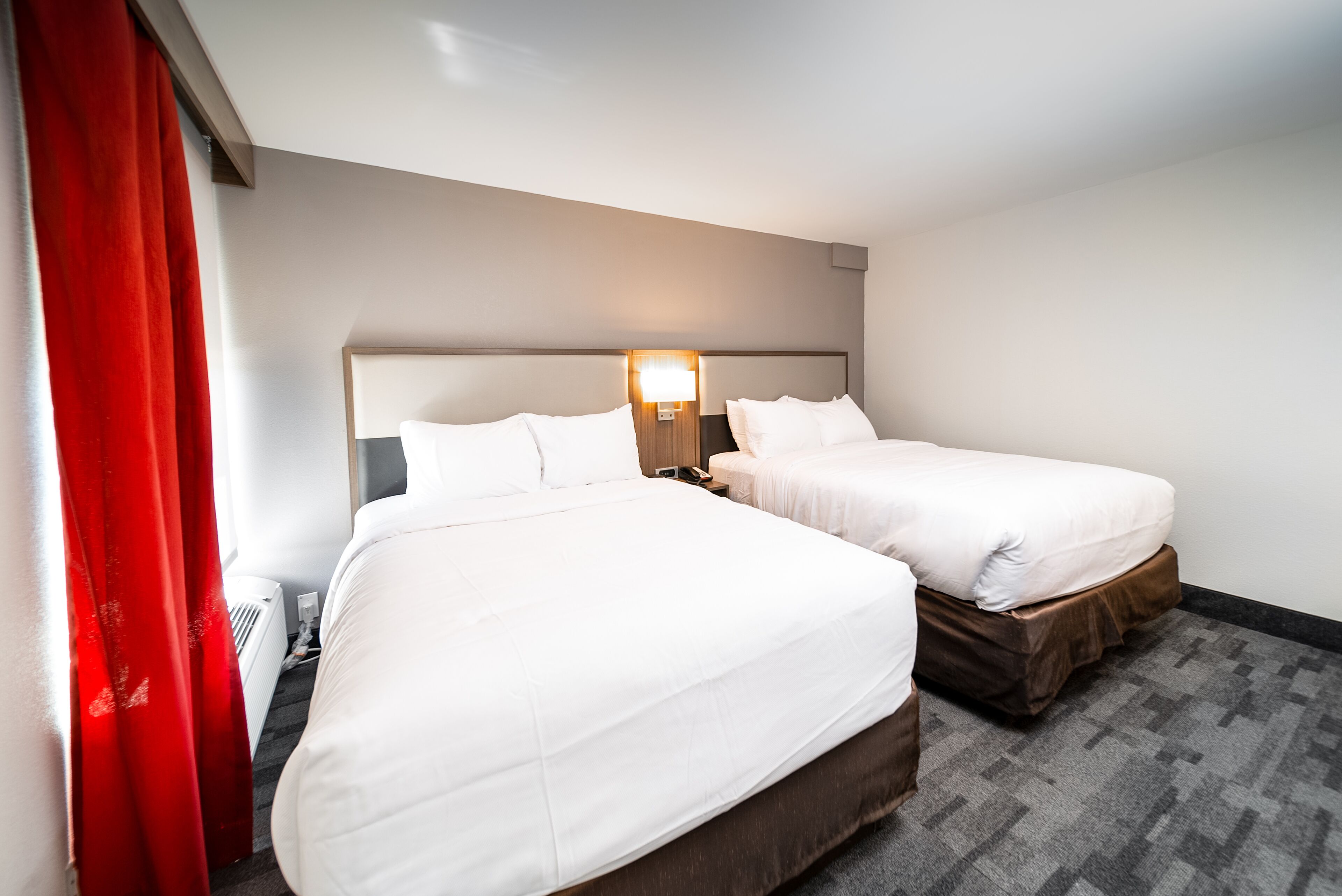 Une chambre d’hôtel avec deux lits, une table de chevet, une lampe et un rideau rouge.