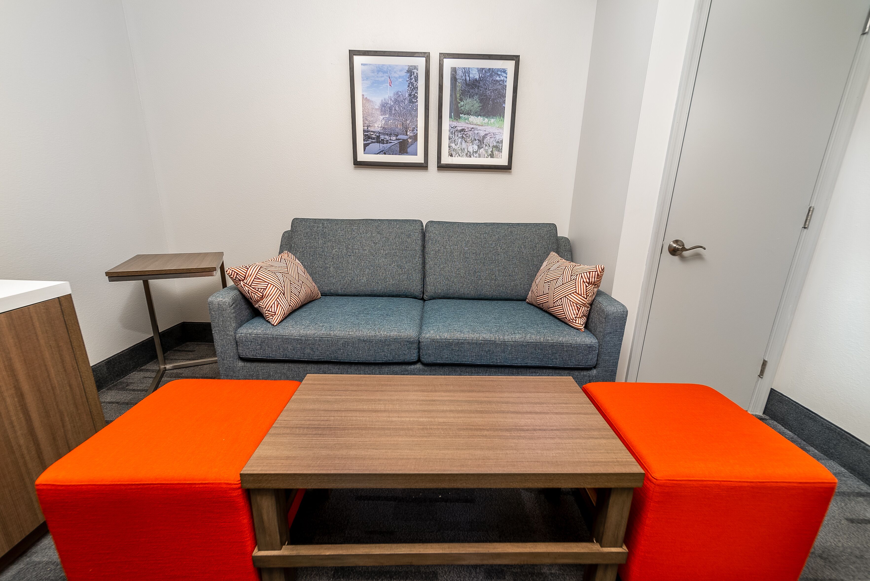 Una habitación con un sofá gris, dos cuadros en la pared y una mesa naranja.