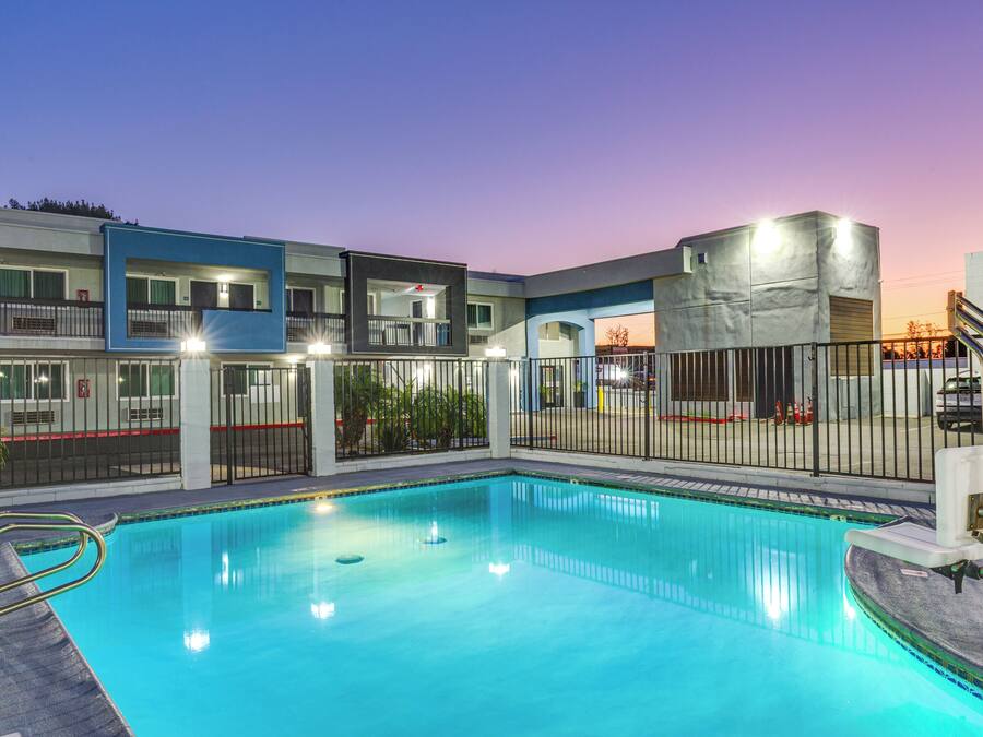 Piscina com escada de metal, cercada por uma grade, e adjacente a um edifício com varandas e janelas.
