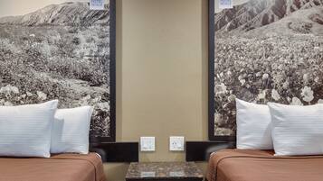 A hotel room with two beds, a small table, and a wall-mounted TV.
