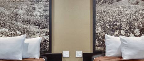 A hotel room with two beds, a small table, and a wall-mounted TV.