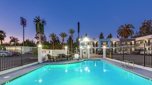 Une piscine entourée d’une clôture, avec des palmiers et un bâtiment en arrière-plan.