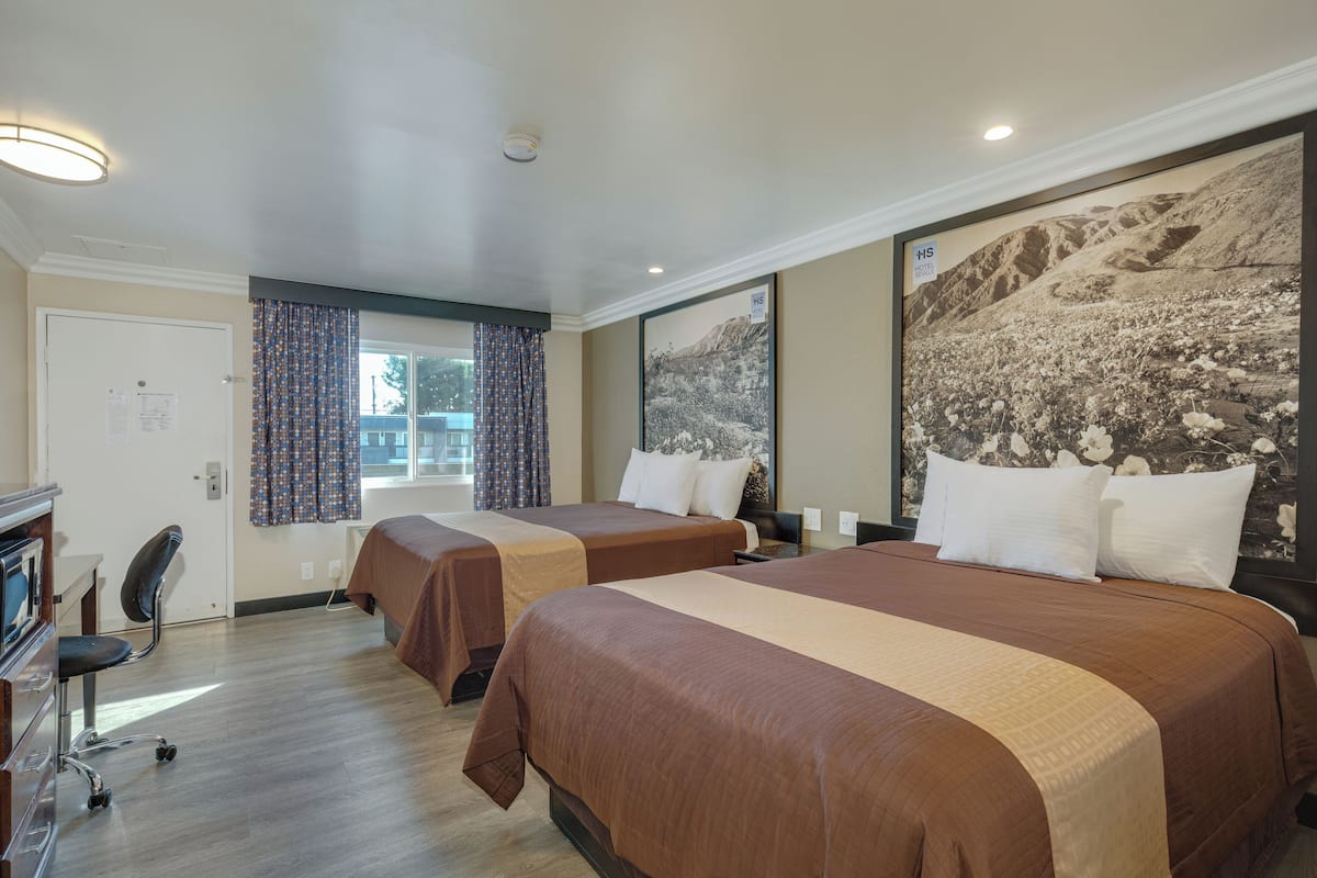 Ein Hotelzimmer mit zwei Betten, einem Schreibtisch mit Computer und einem großen gerahmten Bild an der Wand.