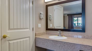 A bathroom with a white door, a granite countertop, a sink, and a large mirror.