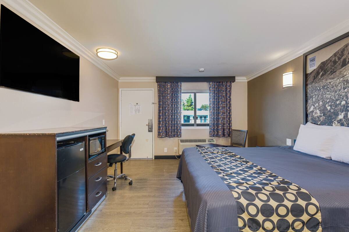 Ein Hotelzimmer mit Bett, Schreibtisch, Sessel, Fernseher und einem Fenster mit Vorhängen.