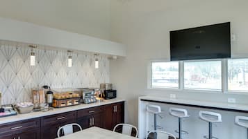 A modern kitchen with a dining area, featuring a white table and chairs, a decorative ceiling light, and a window with a view of the outside.