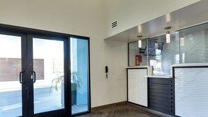 Un hall d’hôtel doté d’une porte coulissante en verre, d’un comptoir d’accueil et d’un parquet en bois disposé en chevrons.