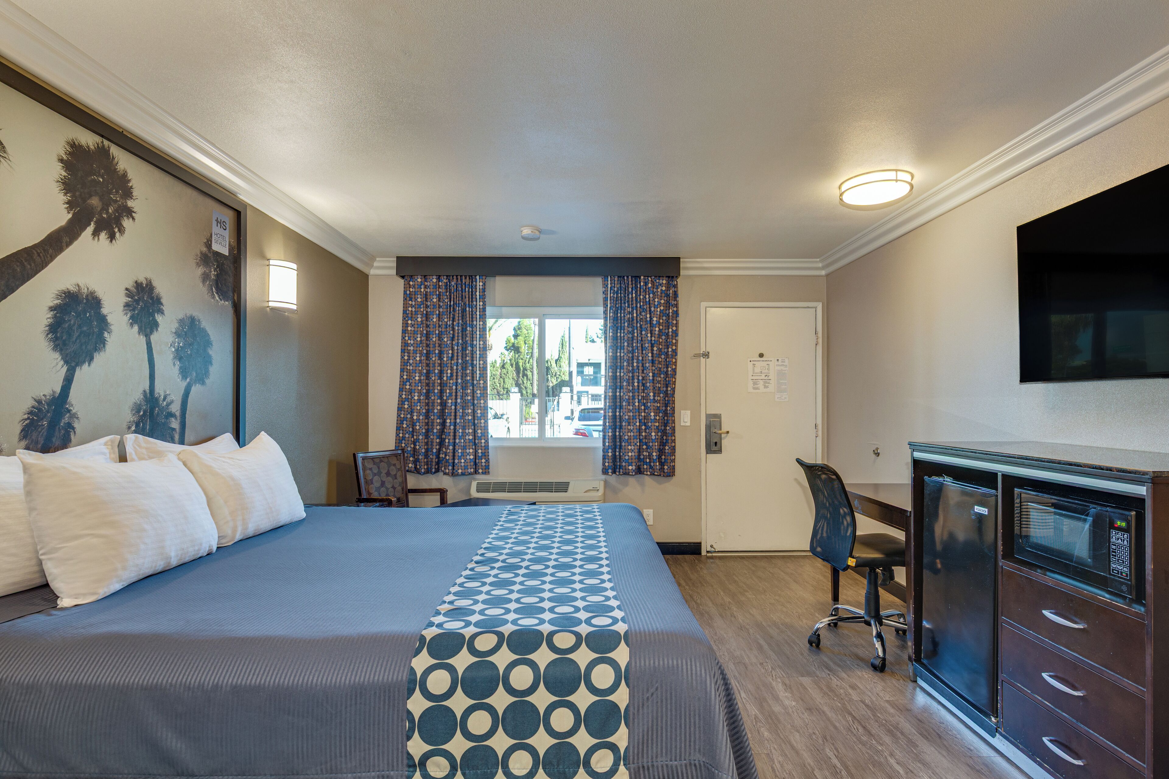 A hotel room with a large bed, a desk with a computer, and a TV on the wall.