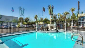 A swimming pool with a fenced area, palm trees, and a Chevron sign in the background.