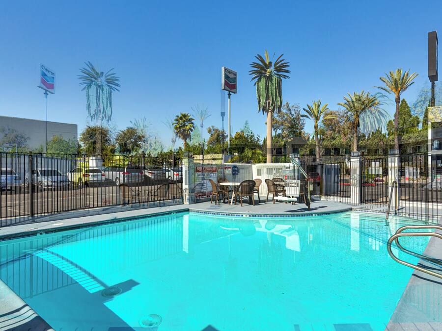 A swimming pool with a fenced area, palm trees, and a Chevron sign in the background.