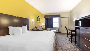 A hotel room with a large bed, a desk, a chair, a television, and a wardrobe.