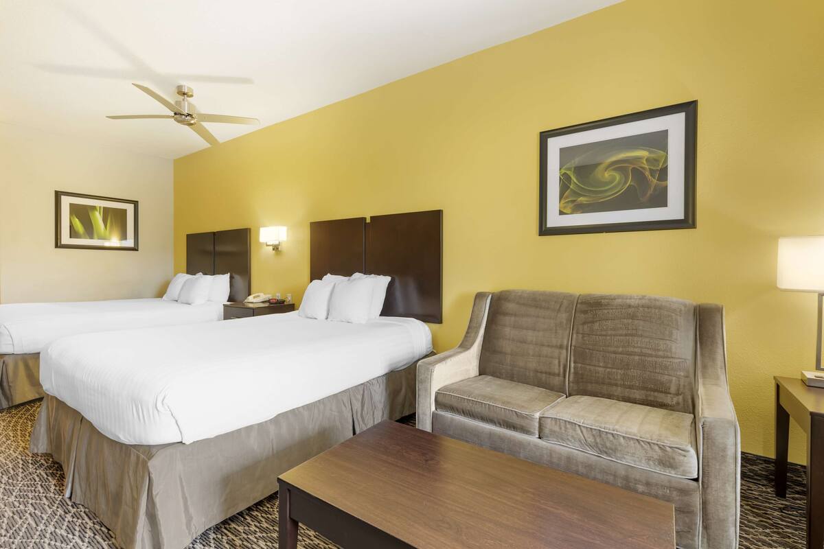 A hotel room with two beds, a sofa, a coffee table, and a ceiling fan.