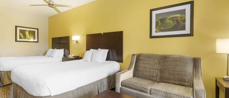 A hotel room with two beds, a sofa, a coffee table, and a ceiling fan.