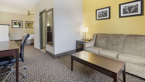Una habitació d'hotel amb un sofà, una taula de cafè, un escriptori amb una cadira i quadres al mur.