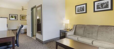A hotel room with a sofa, a coffee table, a desk with a chair, and framed pictures on the wall.