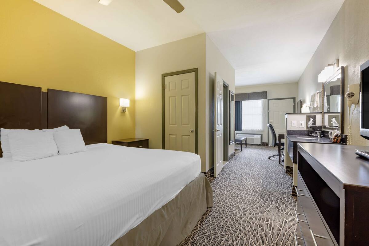 A hotel room with a large bed, a desk with a mirror, and a seating area with a chair and table.